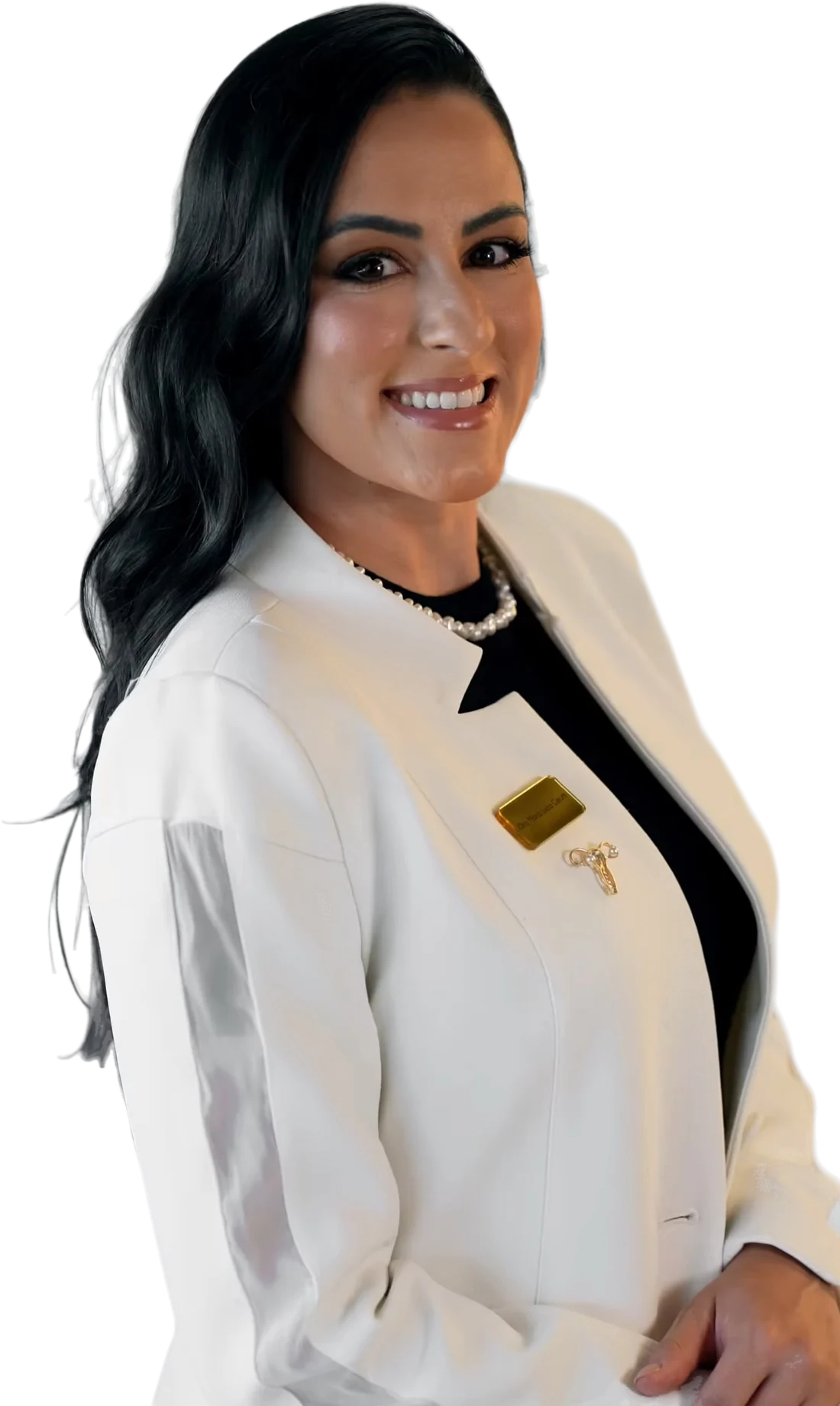 Dra. Mallu Cerutti sorrindo, de blazer branco com plaqueta dourada, broche em forma de útero e colar de pérolas