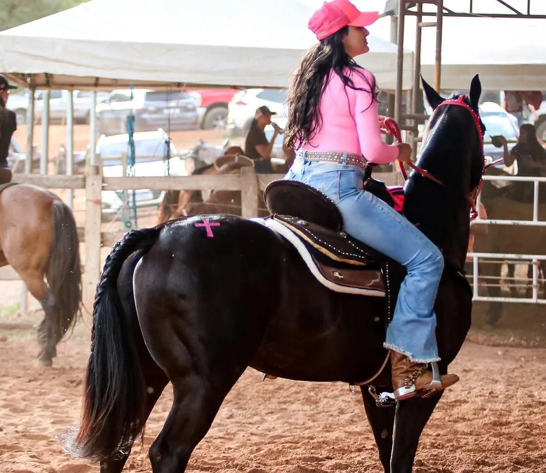Ela de costas, a passo no cavalo preto, perto da cerca da pista